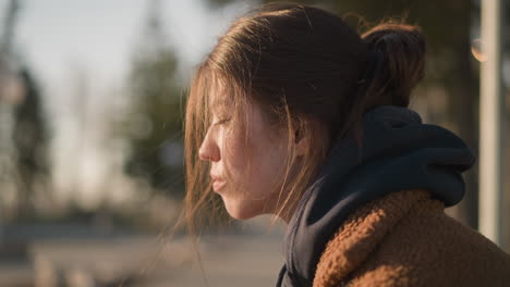 a close-up of a girl wearing a brown coat, with her hair partially covering her face. she looks mournful and lost in thought, her expression reflecting a profound sense of sadness and contemplation