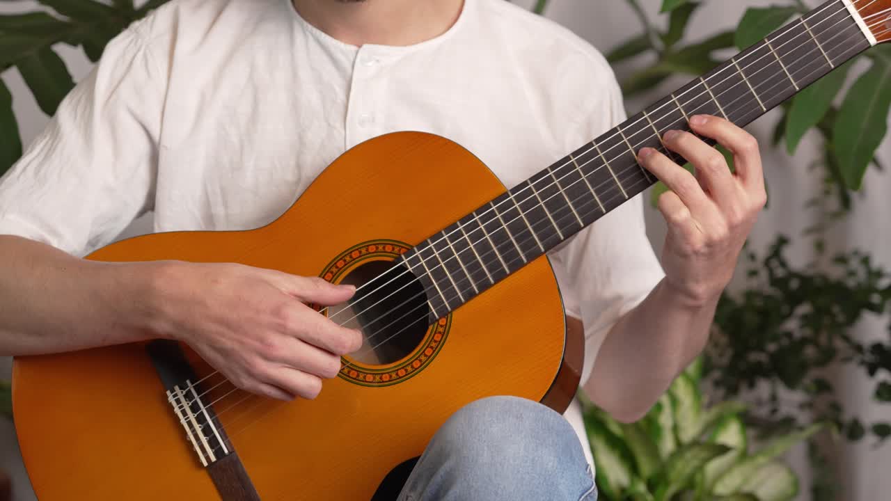 músico tocando guitarra acústica clásica usando los dedos en las cuerdas y el diapasón