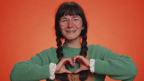 smiling nerd woman makes heart gesture demonstrates love sign expresses good feelings and sympathy