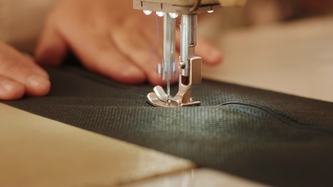 la mano de la costurera está usando una máquina de coser industrial blanca para coser la cremallera de pantalones negros en primer plano.