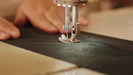 hand of the seamstress is using white industrial sewing machine sew zipper (slide fastener) of crotch black pants close-up.