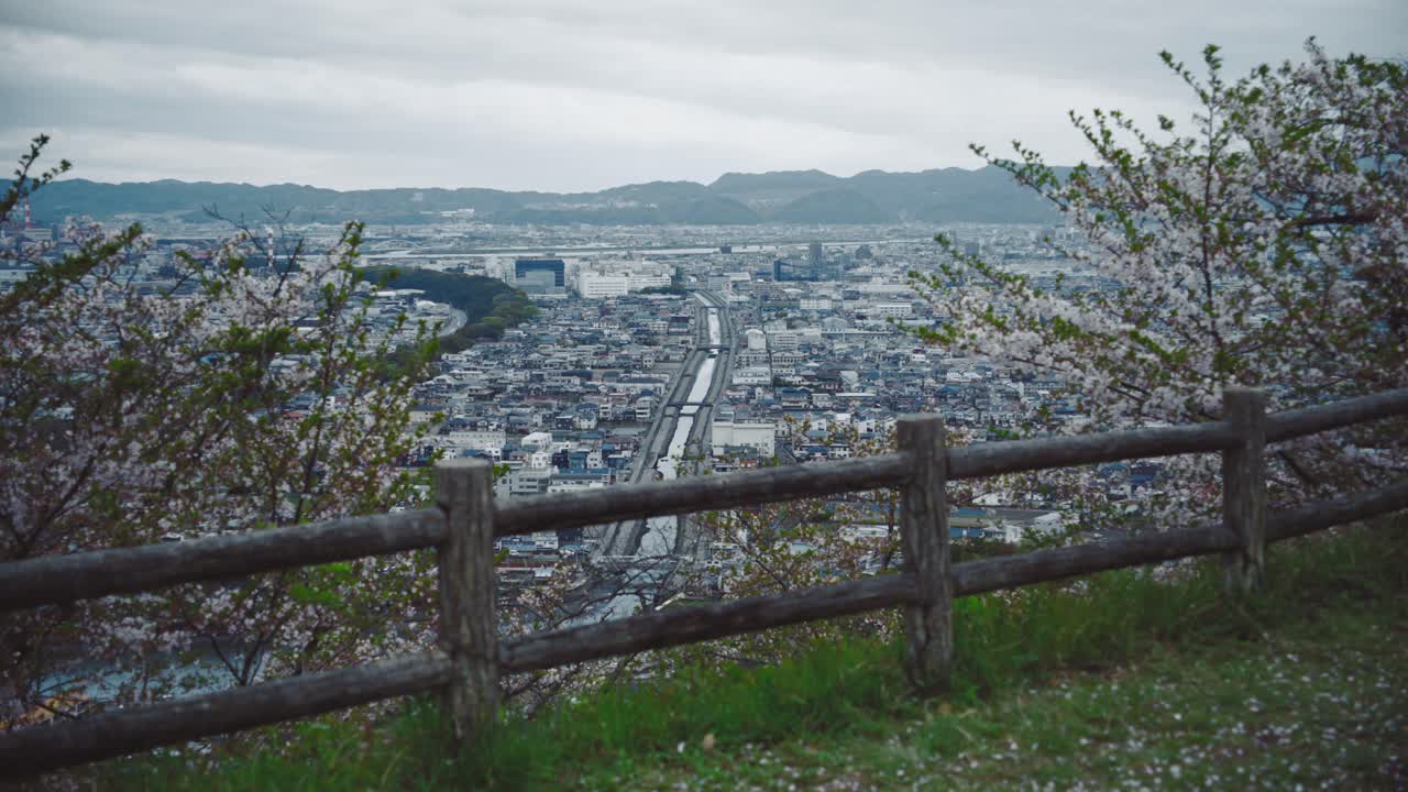 사이카자키 (saikazaki) 를 내려다보는 일본, 구름이 쌓인 날 아래의 도시의 전망을 은 체리 꽃과 함께