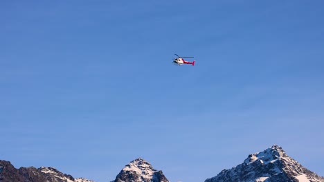 a helicopter flies over snow-capped mountains under a clear blue sky, showcasing serene aerial movement and natural beauty