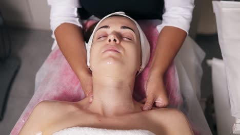 una mujer joven con los ojos cerrados está acostada en el sofá durante el procedimiento cosmético de la cara. un cosmetólogo profesional está haciendo el cuello