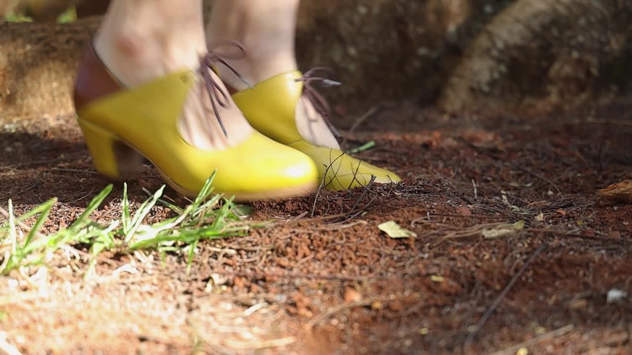 노란색 반부츠 신발을 신은 여성의 발이 자연 속에서 땅바닥에서 두드리고 춤을 춥니다.