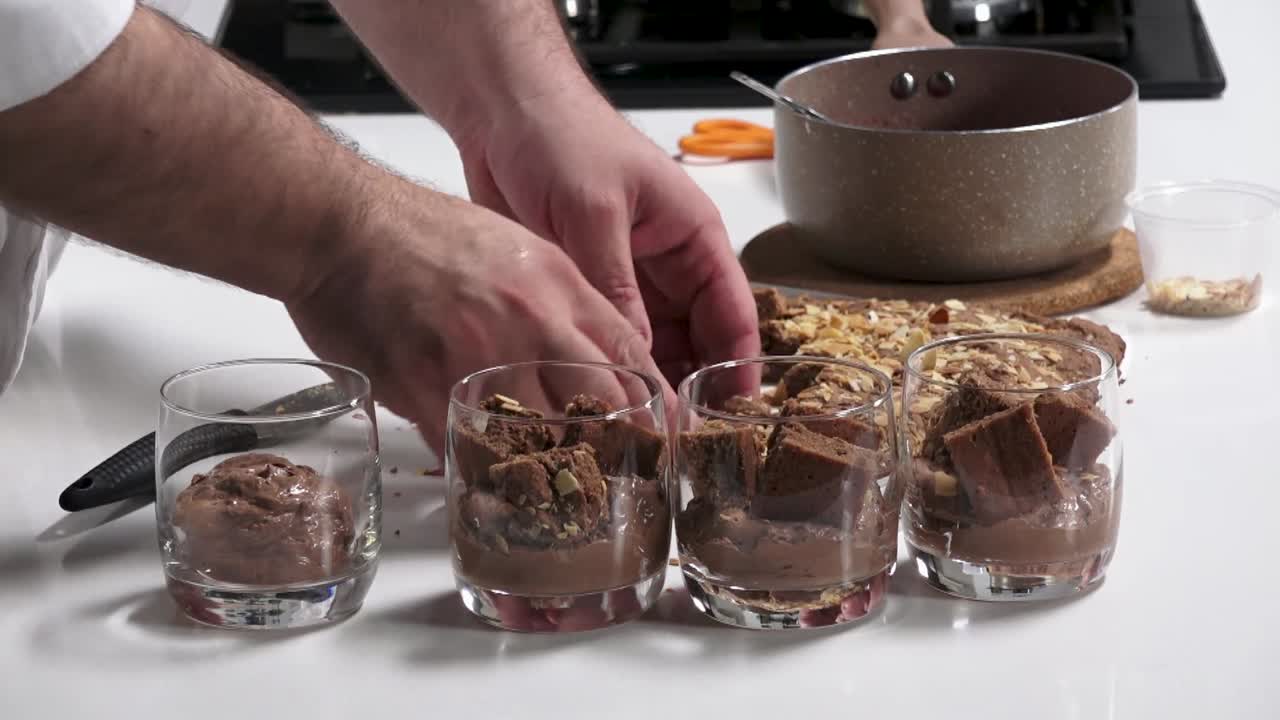 A chef expertly prepares delicious chocolate dessert glasses, layering creamy chocolate and cookie pieces in a well-equipped kitchen setting, showcasing culinary skill