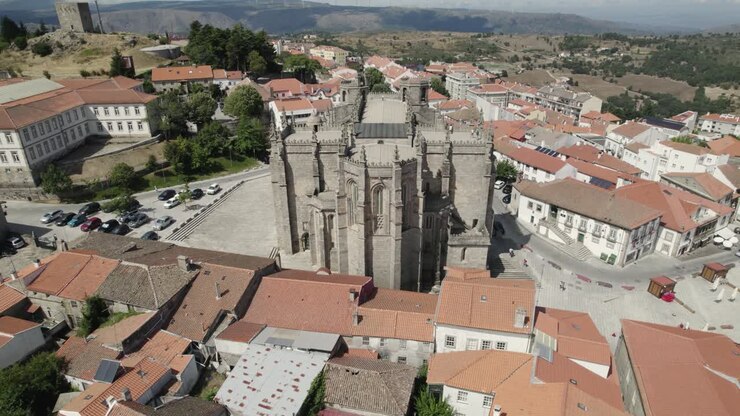 Ripresa aerea all'indietro da un'antica cattedrale in pietra che rivela il magnifico paesaggio urbano di Guarda, Portogallo