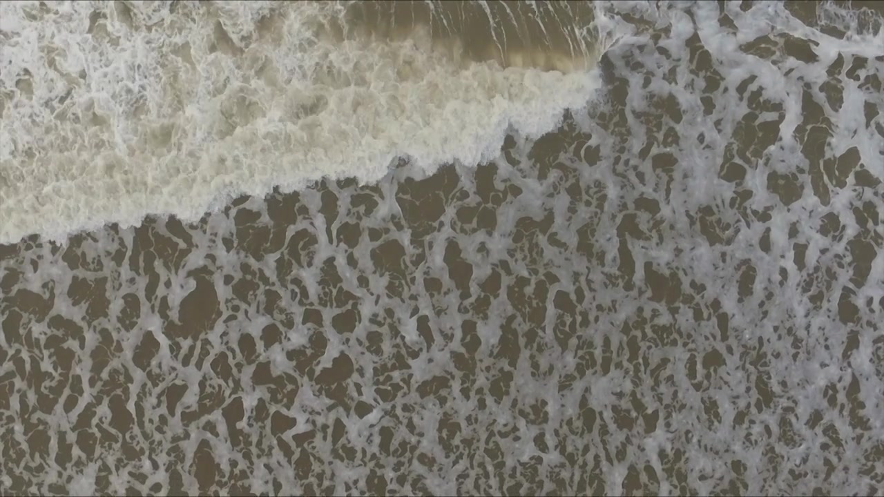 Top down shot of waves crashing onto the beach of Scheveningen in the Netherlands. This is the North Sea, filmed at sunset on October 30 2016. Good backdrop for a title.
