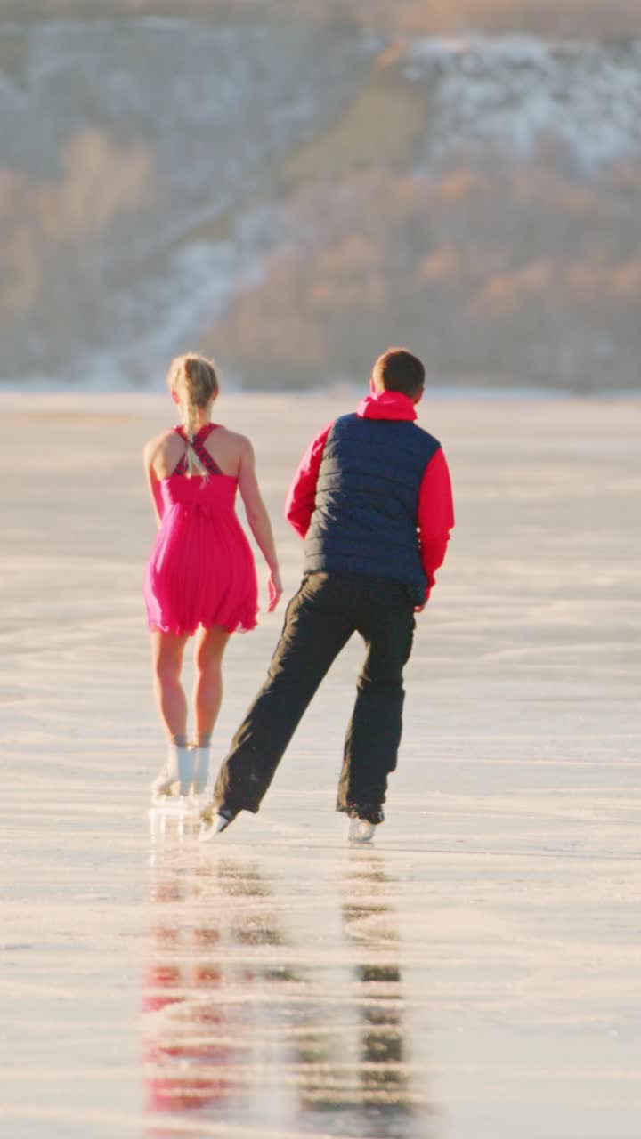 A beautiful winter scene of a young girl in a pink dress ice skating on a frozen lake, accompanied by a man in a red jacket, creating a perfect moment of joy and connection amidst a stunning winter landscape