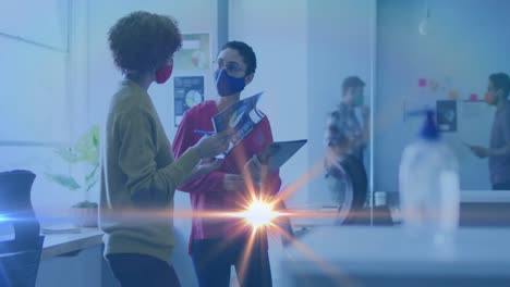 Animation-of-light-spot-moving-against-two-diverse-female-office-colleagues-discussing-at-office