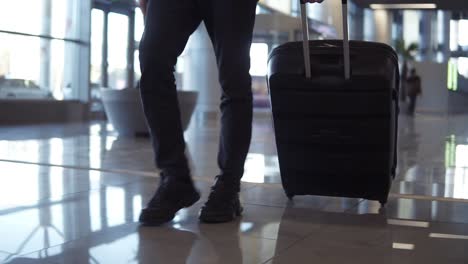 Close-up,-cropped-shot-of-man-legs-with-the-black-baggage-walking-to-the-airport-terminal.-Slow-motion.-Front-view