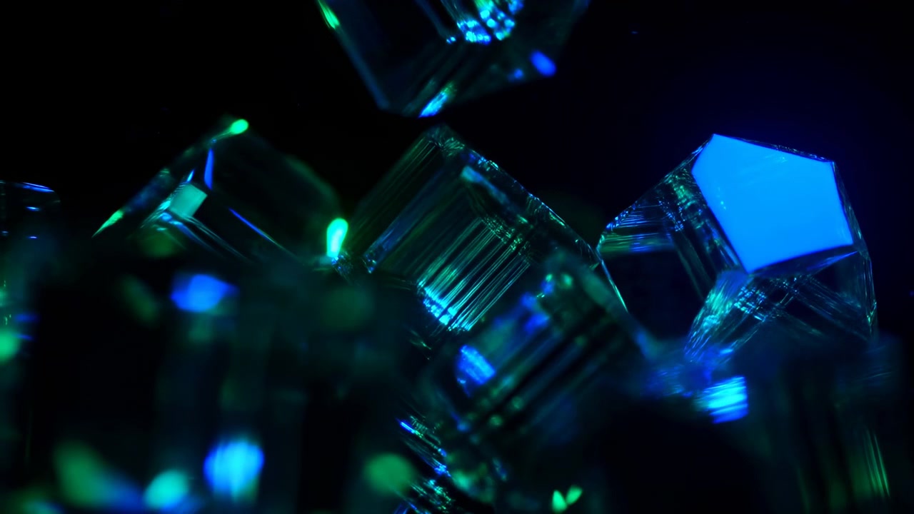 Clear geometric pieces drift through dark macro composition as cyan, blue, and green highlights slide over polished faces, creating layered reflections, blur, and luminous depth.