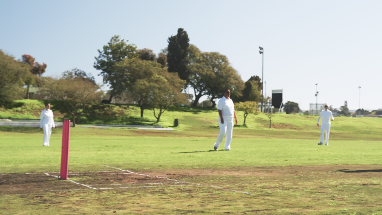 Playing cricket on sunny day, women in white uniforms on grassy field