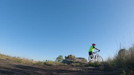 Ciclista-Empujando-Su-Bicicleta-Por-Un-Sendero,-Cielo-Azul-De-Fondo