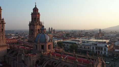 Die-Drohne-Fliegt-Im-Morgengrauen-über-Die-Majestätische-Morelia-Kathedrale,-Während-Das-Warme-Sonnenlicht-Ihre-Historische-Fassade-Durchflutet