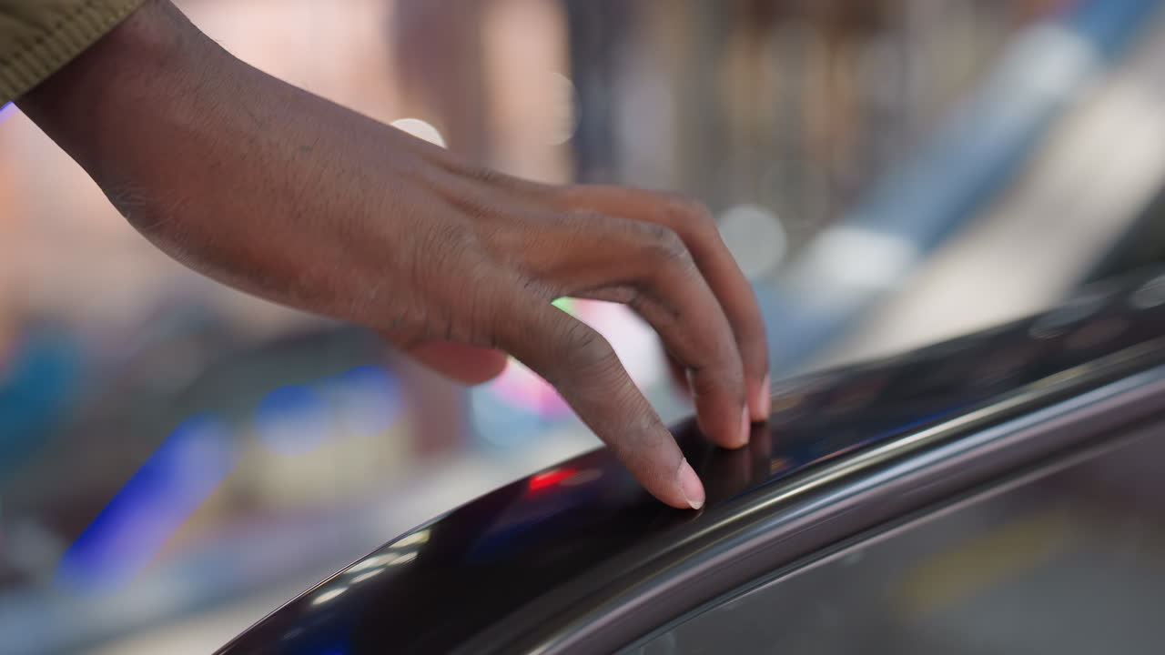 Close up of person tapping escalator rail with finger in brightly lit mall environment showing smooth hand movement against glossy surface with colorful lights and blurred background