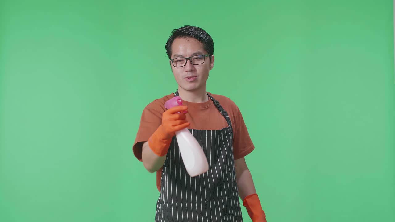 녹색 스크린 스튜디오에 서 있는 동안 총으로 불기 전에 아프론 스프레이를 가진 아시아 남성 집주인