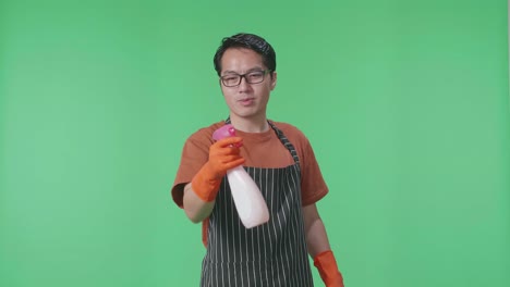 녹색 스크린 스튜디오에 서 있는 동안 총으로 불기 전에 아프론 스프레이를 가진 아시아 남성 집주인