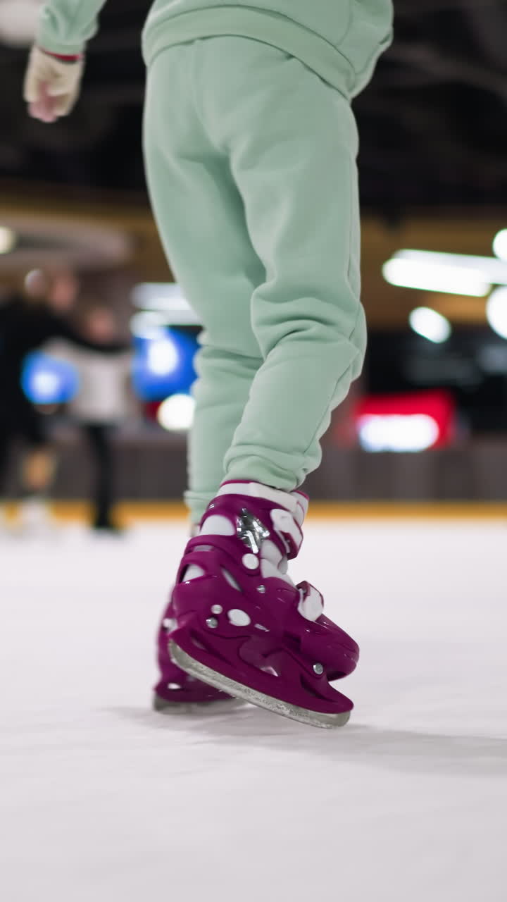 primer plano de alguien patinando en patines de hielo púrpura con pantalones de color ceniza en una pista de hielo, con otros patinadores en el fondo