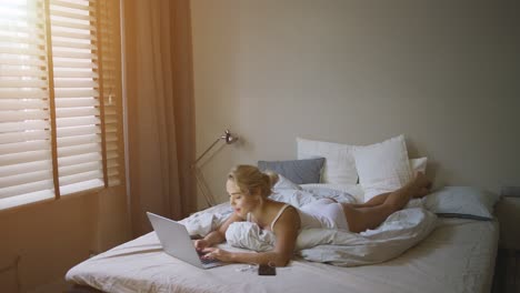 sensual young woman in white tank top and panties lying on bed near laptop