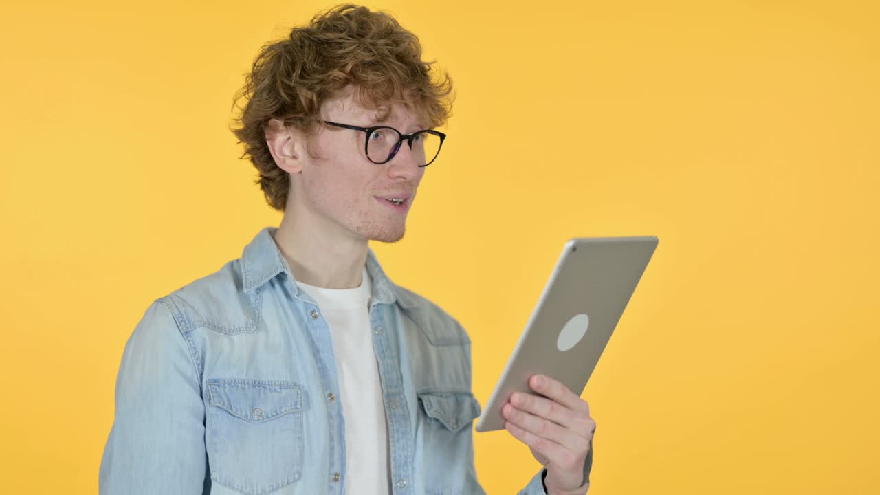 Video Call on Tablet by Redhead Young Man,  Yellow Background