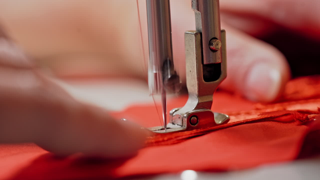 Process of sewing machine working with red fabric. Woman's hands at work on metal sewing machine with bright red material. Close-up