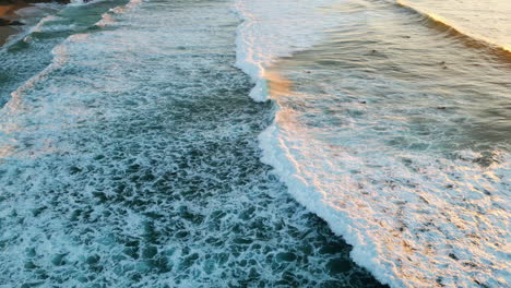 drone view foamy sea splashing at sunset sunlight. aerial waves rolling to shore