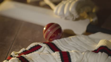 Cricket-Stillleben-Mit-Nahaufnahme-Von-Schlägern,-Ballhandschuhen,-Stümpfen,-Pullover-Und-Kautionen,-Die-Auf-Einer-Holzoberfläche-In-Der-Umkleidekabine-Liegen-4