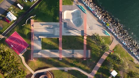 Aerial-bird's-eye-shot-view-of-skatepark-design-rural-town-travel-tourism-basketball-court-concrete-ramps-break-wall-Port-Macquarie-caravan-park-NSW-Mid-north-Coast-Australia-4K