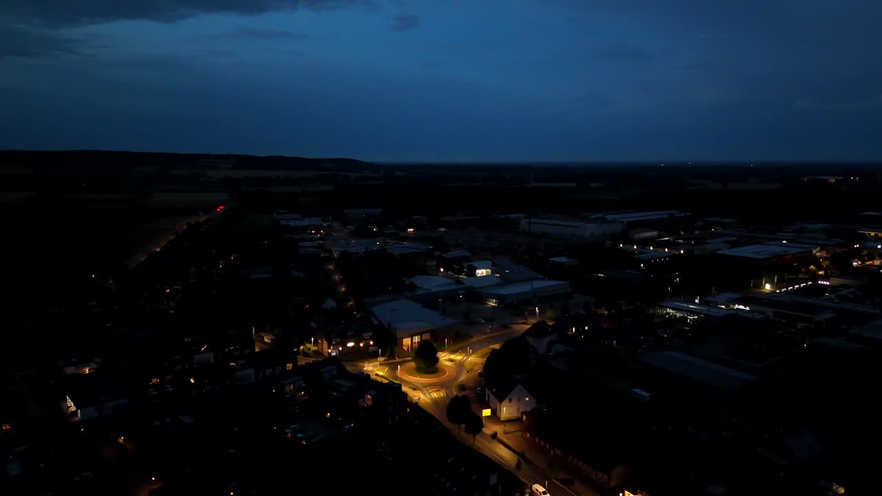 Zářící lucerna na kruhovém objezdu amerického města v noci. Široký letecký záběr. Scéna za soumraku s tmavě modrou oblohou o půlnoci. Domy a osvětlená ulice. Poklidná scéna ze sousedství.