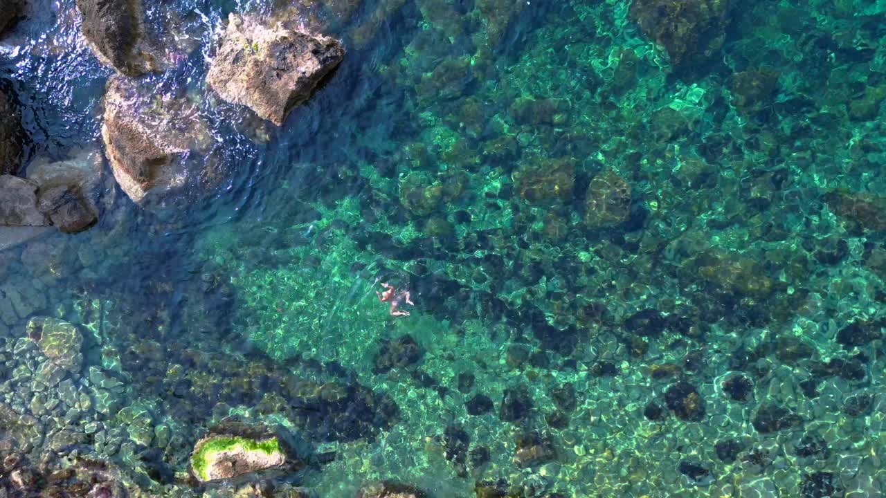 two tourists swimming in the transparent waters of Ibiza, Spain. vertical bird's eye view drone