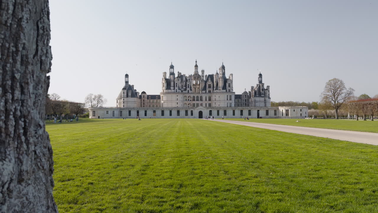 Majestic French Renaissance castle with tourists, trees, and a bright clear sky