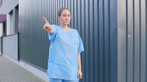 woman wearing blue lab coat saying no with her finger while shaking her head, static