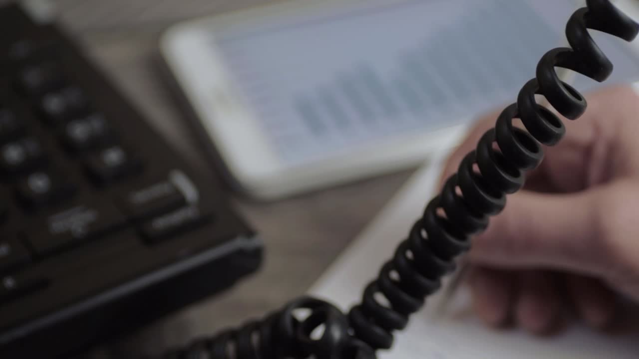 Busy person using a phone writing notes with a graph on a tablet