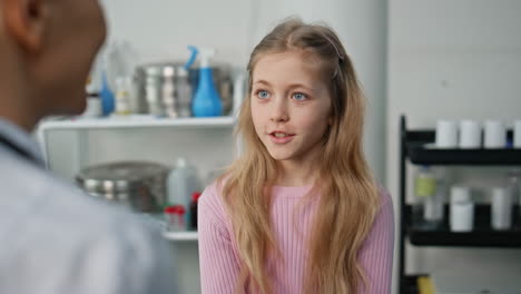 Cute girl visiting doctor in childcare clinic closeup. Pediatrician talking kid