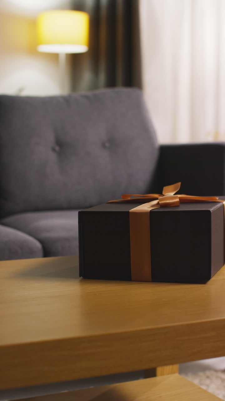 вертикальное видео человека, кладущего подарок в упакованную в подарок коробку, украшенную лентой, на стол в гостиной