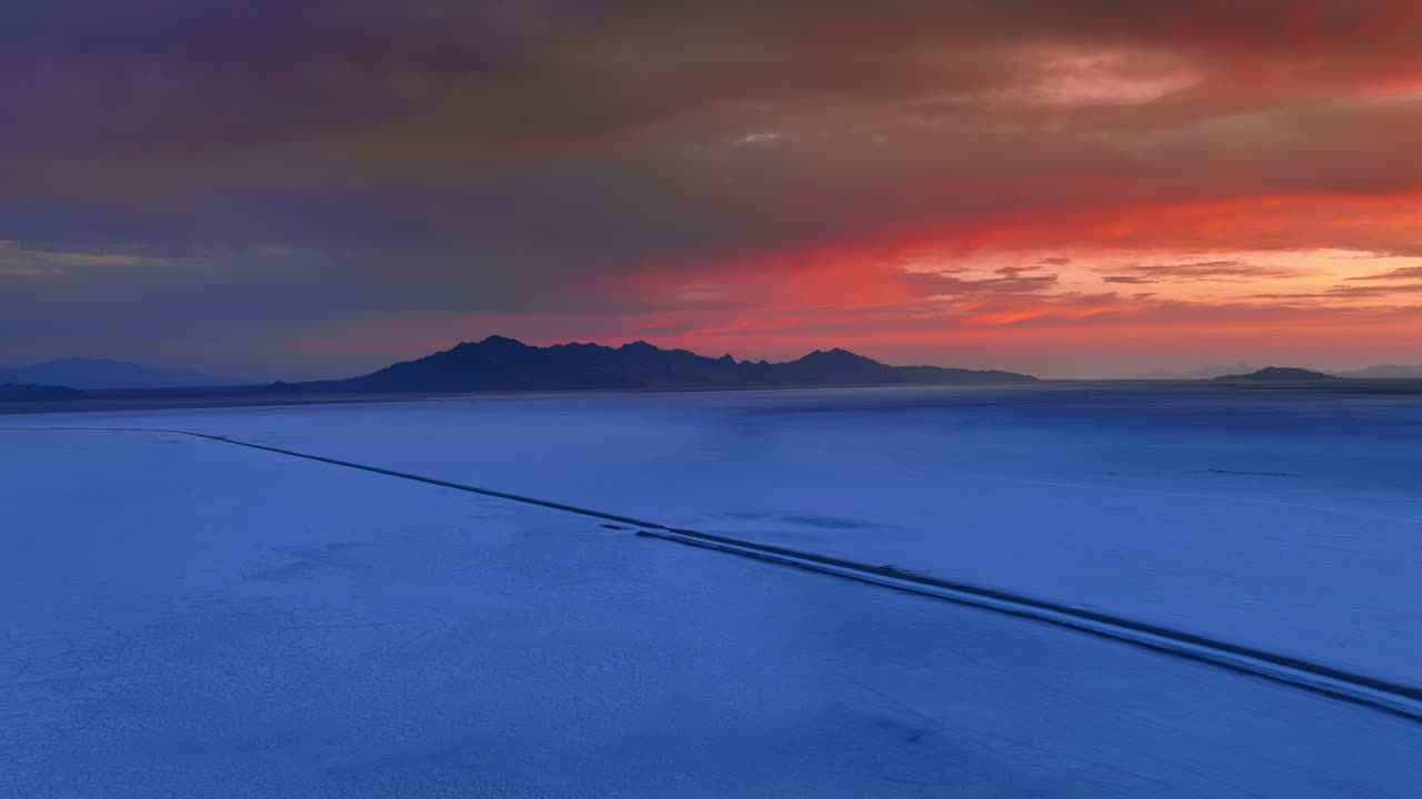 Approaching the road crossing vast salty valley in Bonneville Salt Flats, Utah, United States. Dramatic red sky above the scenery