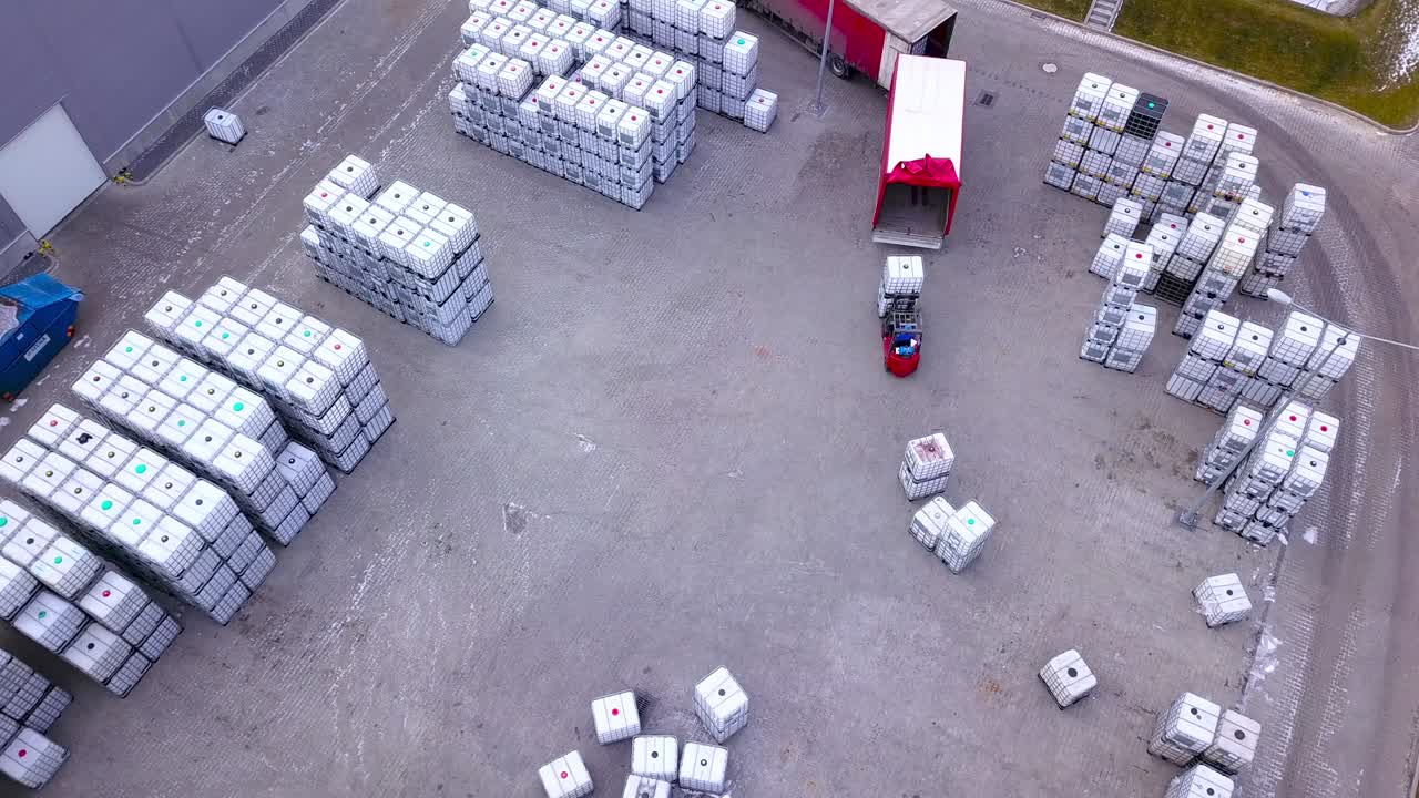 Forklift trucks move between large shelves at outside warehouse and load pallets.Aerial. Drone shot