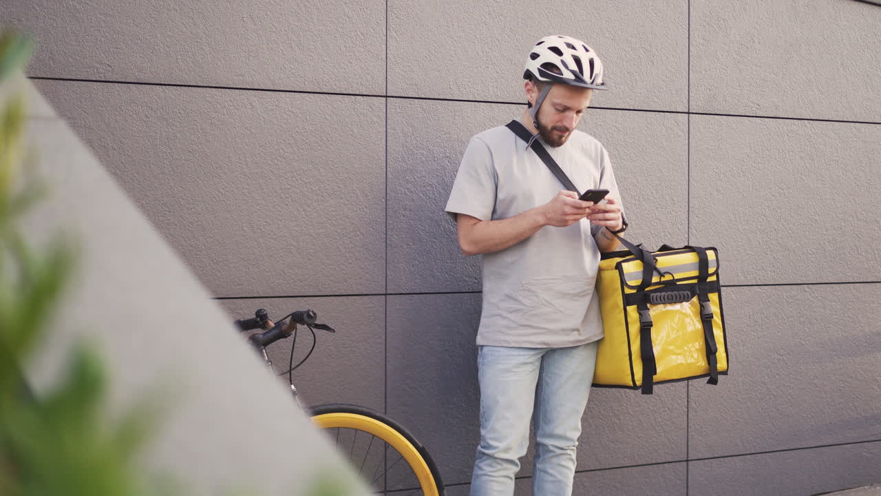 Food Delivery Man With A Thermal Backpack Consults An Order On His Smartphone