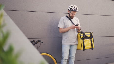 food delivery man with a thermal backpack consults an order on his smartphone