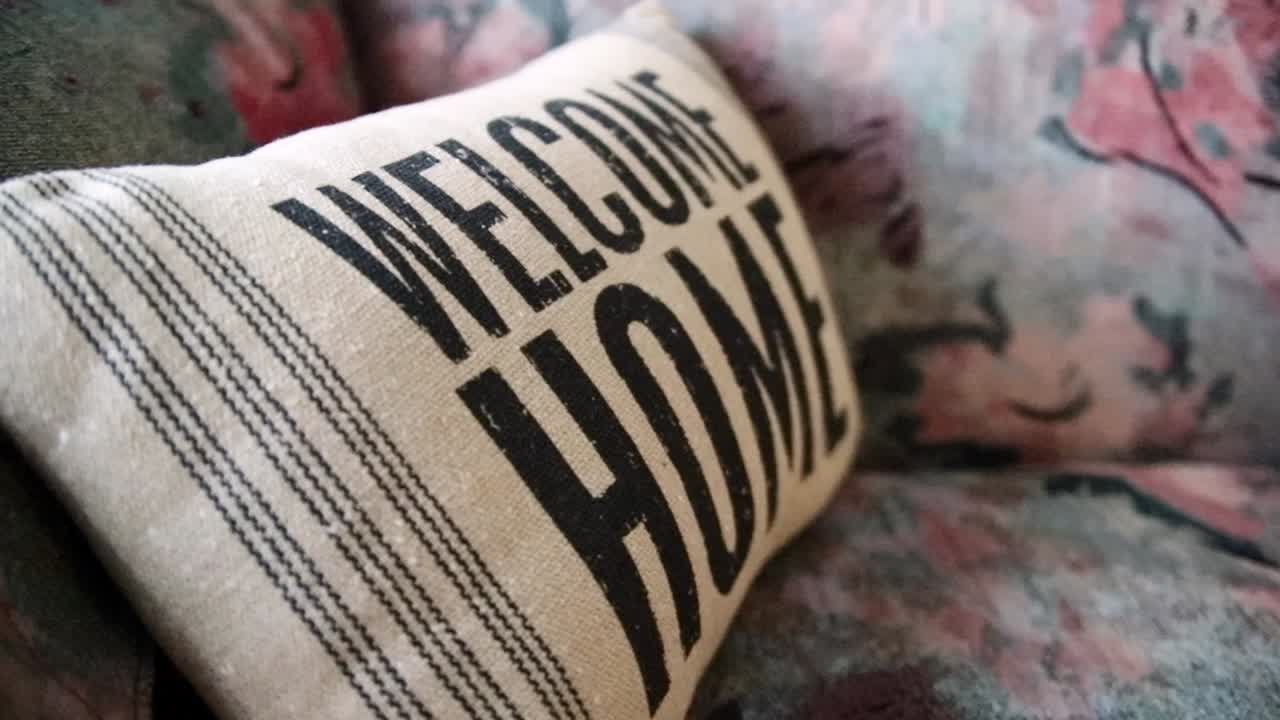 almohada de aspecto antiguo con "bienvenido a casa" impreso en ella