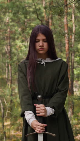 dark-haired young woman in forest plunges sword into ground