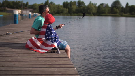 father and son taking a selfie on a lake pier