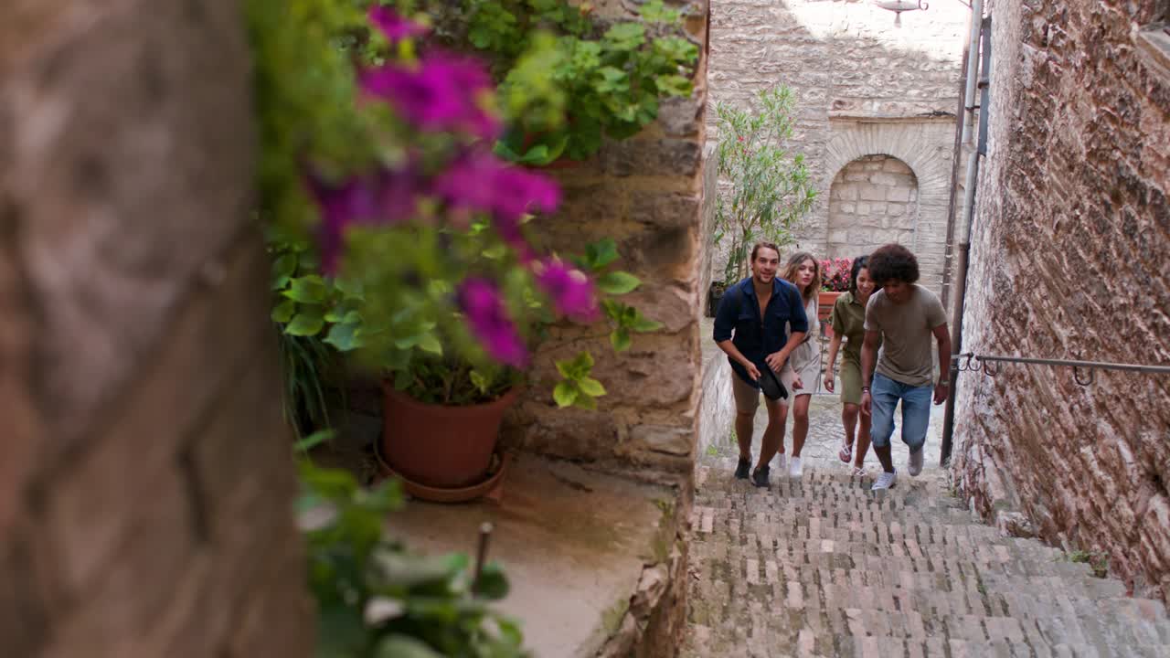 cuatro amigos felices subiendo escaleras. gente turística caminando y corriendo por pequeñas escaleras callejeras visitando la ciudad rural de spello.