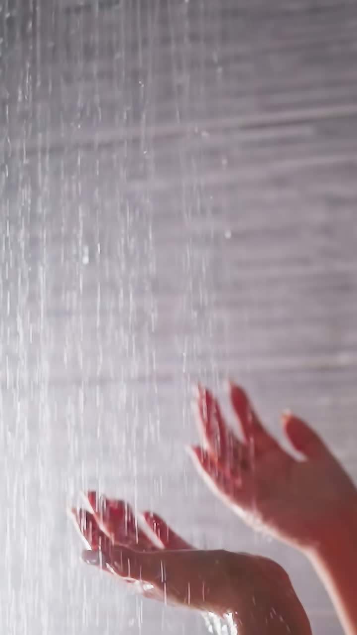 la mujer pone las manos bajo los sprays de ducha en el baño. la dama contemplativa toca el flujo de líquido caliente por las elegantes palmas en el lavabo. relajación en el spa en casa