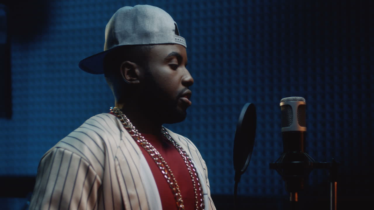 헤드폰을 끼고 어두운 사운드 스튜디오에서 노래를 녹음할 준비를 하는 모자 가수의 젊은 남자를 닫습니다