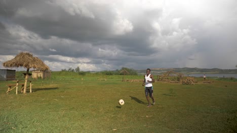 Wide-shot-of-African-youth-doing-kick-ups-with-a-football-on-a-beach-by-the-shores-of-Lake-Victoria-with-storm-clouds-moving-in