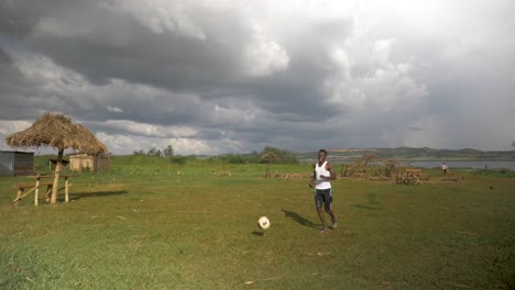 wide shot of african youth doing kick ups with a football on a beach by the shores of lake victoria with storm clouds moving in