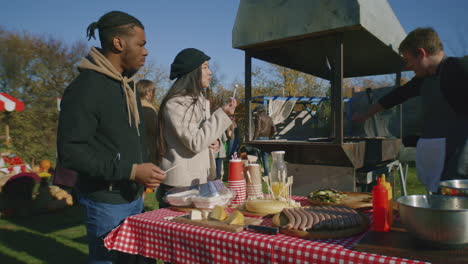 multi ethnic couple at autumn fair multi ethnic couple at autumn fair or farmers markets asian woman and african american man trying cheese man cooks meat on grill holder of point of sale system outdoors picnic slow motion