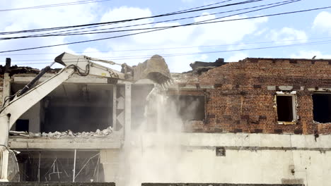 excavator demolishes damaged old building to clear area for reconstruction or new urban development